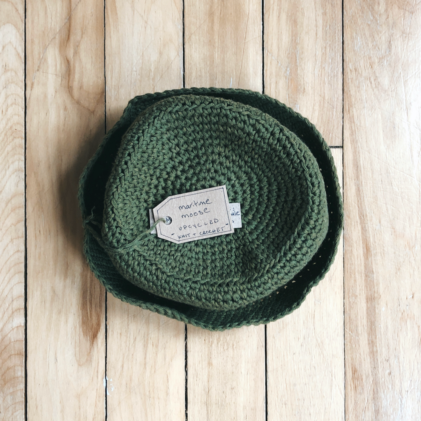 View from above on the green baby bucket hat. The tag is sitting on top of the circular top of the bucket hat, and the brim is folded up around the hat.
