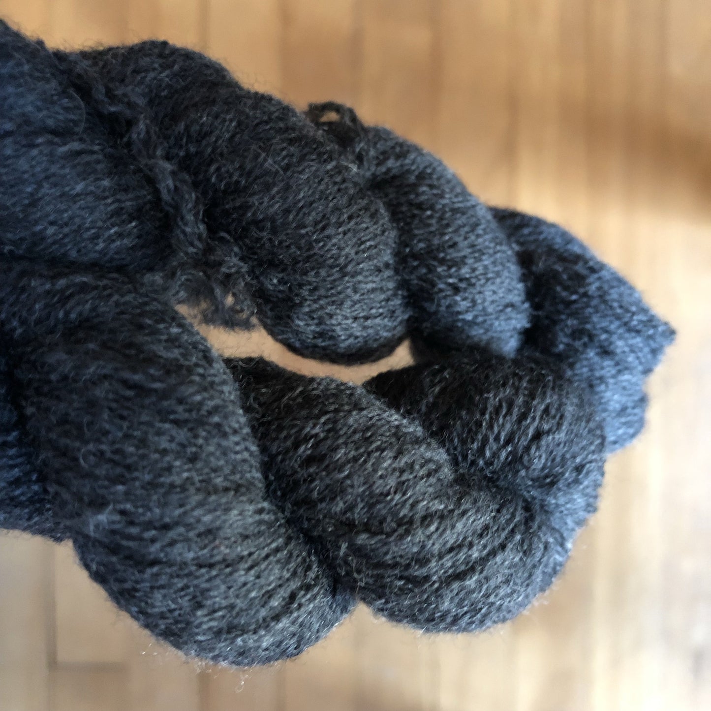Up close shot of the thin merino wool yarn. It is a dark charcoal grey and quite dense.
