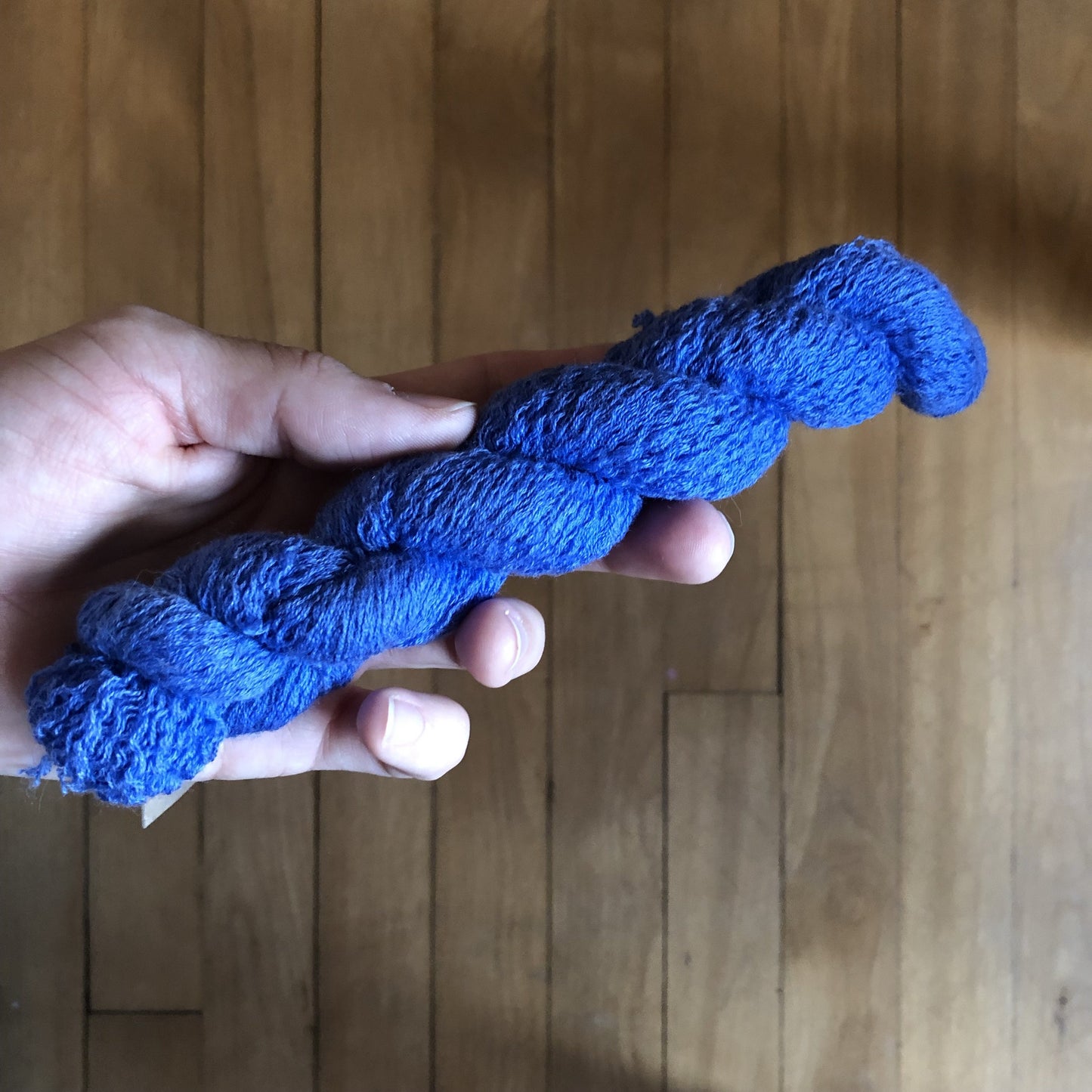 A hand holding a mini skein of cobalt blue cotton/wool yarn.