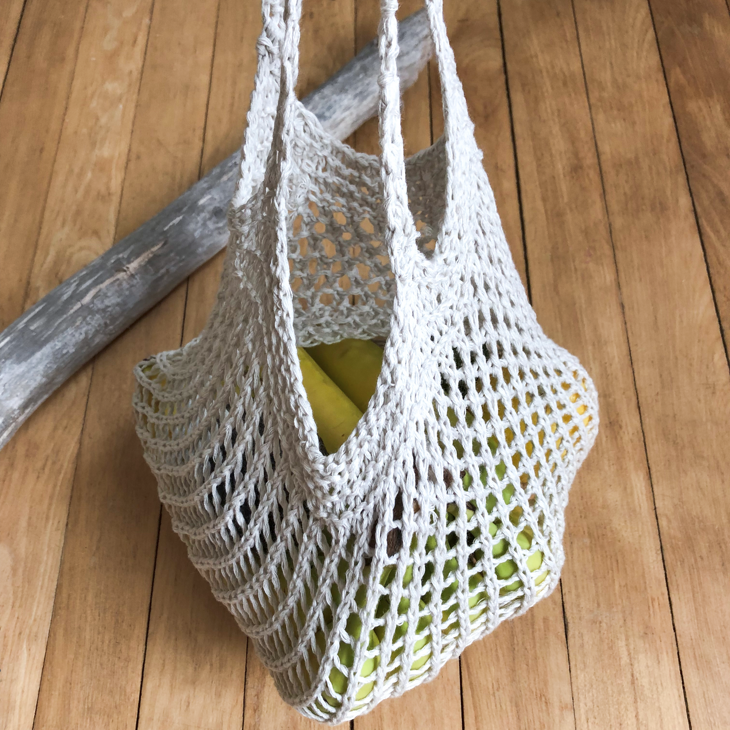 A salt of the earth produce bag size large holding various fruit. Picture shows stretchy holes in the bag and thick knitted rim around the opening where the two handles are attached.