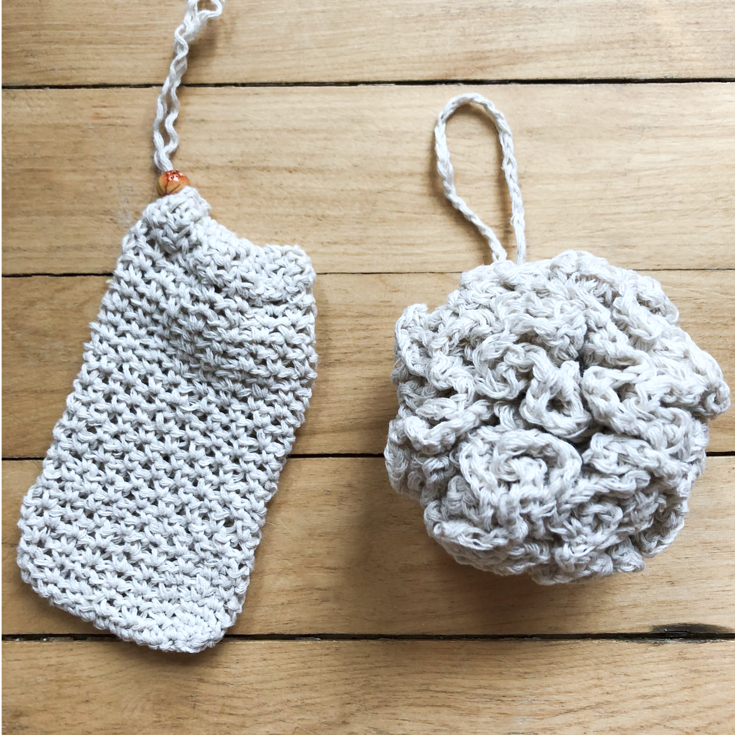 The upcycled soap saver and upcycled bath pouf lay next to each other against a wooden background. Each of them has a loop attachment to hang from a shower hook or bath faucet.