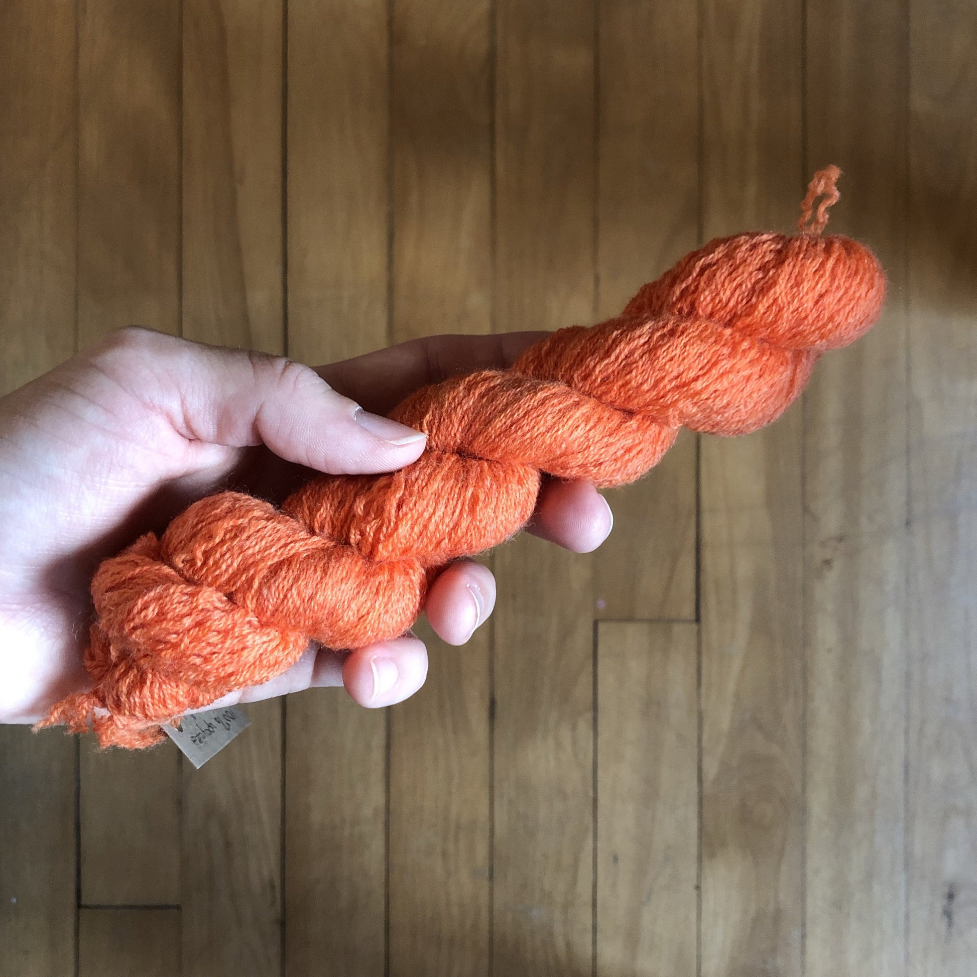 A hand holding a mini skein of bright orange merino wool.