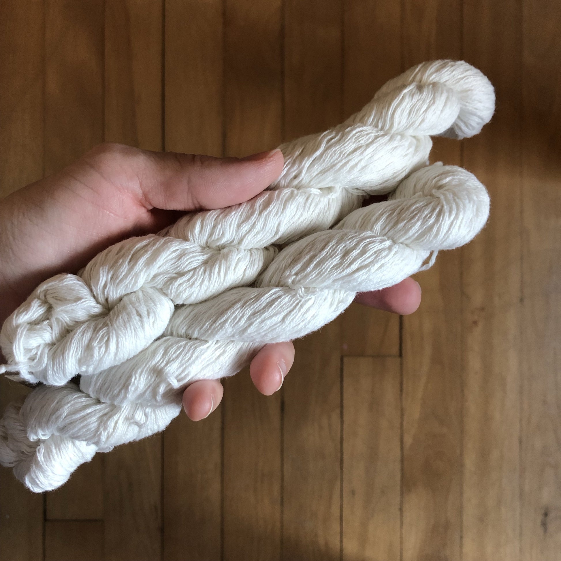 A hand holding two mini skeins of upcycled white cotton yarn.