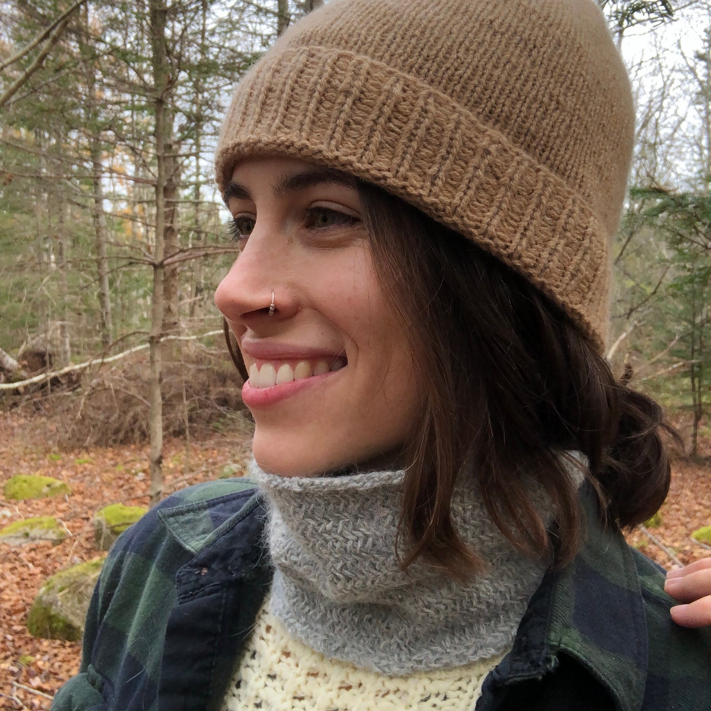 Pam wearing the grey nor'easter neck warmer paired with the cashmere toque and smiling, looking off to the left of the camera. The upcycled buff looks thin but cozy and woolen.