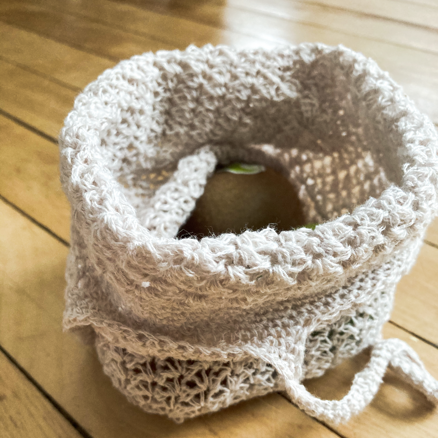 A salt of the earth produce bag size small holding some kiwis. The bag is sitting on the floor with the top folded over, revealing the fruit inside.